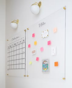 a white board with post it notes on it next to two lamps and a wall mounted calendar