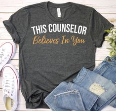 a t - shirt that says, this counselor believe in you on it next to jeans and sneakers