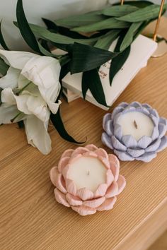 two small candles sitting on top of a wooden table next to flowers and a box