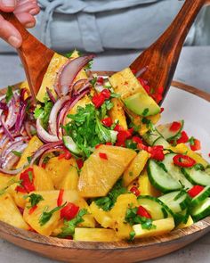 a wooden bowl filled with pineapple, cucumber and red onion salad on top of a white plate