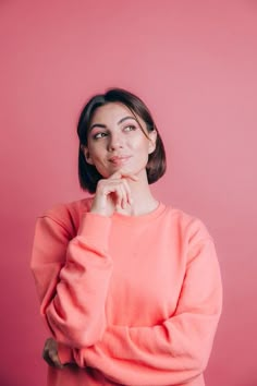 a woman in an orange sweater is posing for the camera with her hand on her chin