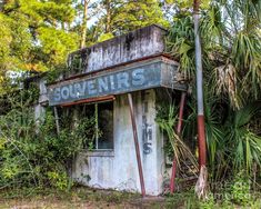 an old run down building sitting in the middle of some grass and trees with graffiti on it