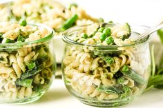 two glass jars filled with pasta and vegetables on top of a white table next to green beans