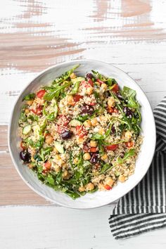 a white bowl filled with salad on top of a wooden table next to a black and white towel