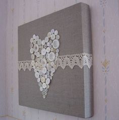 a canvas with buttons and lace on it hanging on the side of a wall in a room