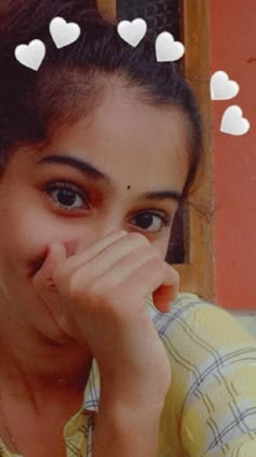 a girl with her hand on her face looking at the camera and hearts above her head