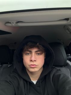 a young man sitting in the back seat of a car wearing a hoodie and looking at the camera