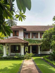 a white house with brown shutters and green plants on the front lawn, surrounded by lush greenery