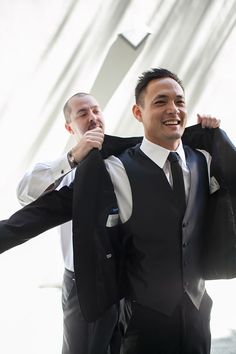 two men in suits are holding on to their ties and smiling at the camera while another man holds his jacket over his shoulder