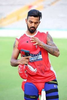 a man in red shirt and knee pads holding a cell phone on field with grass