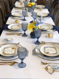 the table is set with blue and white dishes, silverware, and yellow flowers