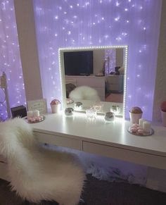 a vanity table with a mirror and lights on the wall next to it in front of a purple curtain