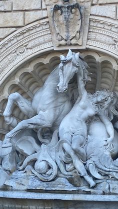 a statue of three horses and two men on the front of a building with an arch