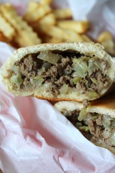 a close up of a sandwich with meat and vegetables in it next to french fries