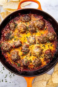 a skillet filled with meatballs and cheese surrounded by tortilla chips