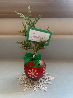 a small red ball with a green bow on it and a name tag attached to the top