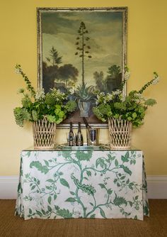 a painting hanging on the wall above a table with two vases filled with flowers