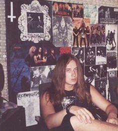 a man sitting in front of a wall covered with pictures and posters on it's walls