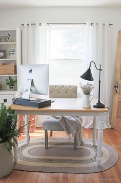 a desk with a computer on top of it next to a potted plant in front of a window