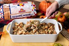 a person cutting into a casserole dish on a table with fall leaves and pumpkins