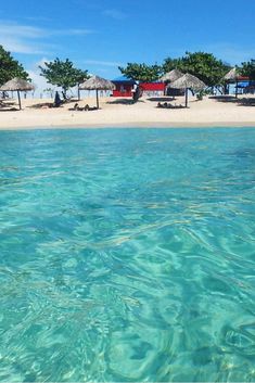 the water is crystal blue and clear, with umbrellas on the beach in the background