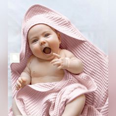 a baby wrapped in a pink blanket laying on top of a white sheet with its tongue out