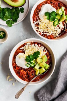 two bowls of chili with avocado, cheese and sour cream on the side