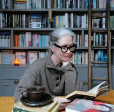 an older woman sitting at a table in front of a book shelf filled with books