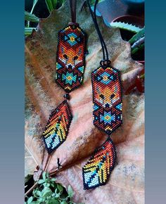 three beaded necklaces sitting on top of a leaf covered ground next to plants