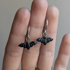 a pair of black bats dangling from silver hoop earrings on someone's hand,