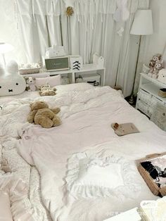 there is a teddy bear laying on the bed in this room with white walls and curtains