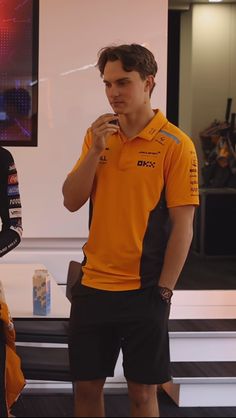 a man in an orange shirt and black shorts standing next to another man with his hand on his mouth