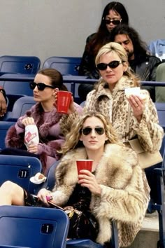 two women sitting next to each other in the stands at a baseball game wearing sunglasses and fur coats