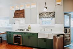 a large kitchen with green cabinets and white counter tops, an island sink and dishwasher