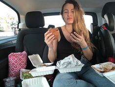 a woman sitting in the back seat of a car with food on her hands and other items