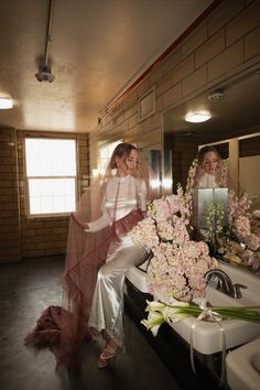 two women are sitting in front of a mirror with flowers on the counter next to them