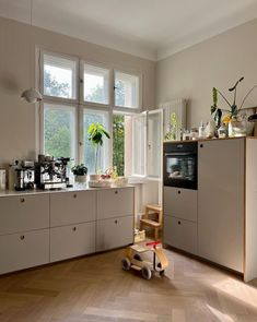 a kitchen with wooden flooring and white cupboards next to a window filled with potted plants