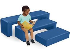 a little boy sitting on a blue bench reading