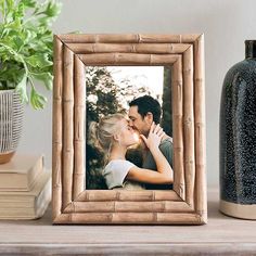 a couple kissing in front of a bamboo frame on a shelf next to a vase