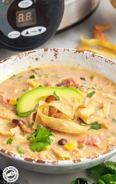 a bowl of soup with tortilla chips and avocado on the side