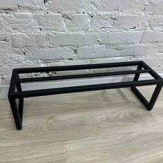 a black metal and glass coffee table against a white brick wall with wood flooring