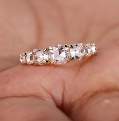 a woman's hand holding a gold ring with three stones on it and the middle one is white