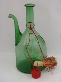 a green glass vase with a red string tied around it and a small piece of wood next to it