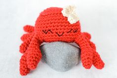 a crocheted red hat with white flower on top sits next to a rock