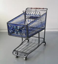 an empty shopping cart sitting on top of a gray floor next to a white wall