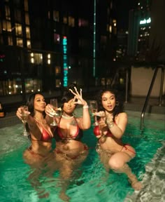 three beautiful women in bikinis sitting in a pool drinking wine and posing for the camera