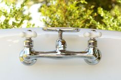 two chrome faucets on the side of a white bathtub with trees in the background