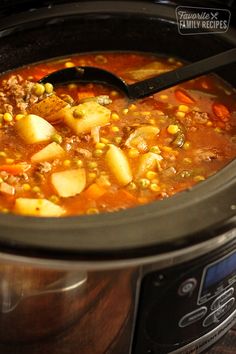 a crock pot filled with stew and potatoes on top of a table next to a spoon