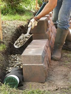 a person is placing rocks in the ground near a brick bench and garden hoses