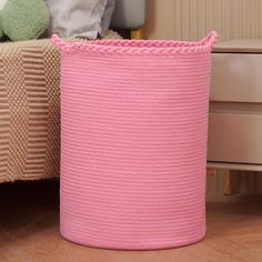 a pink basket sitting on the floor next to a bed